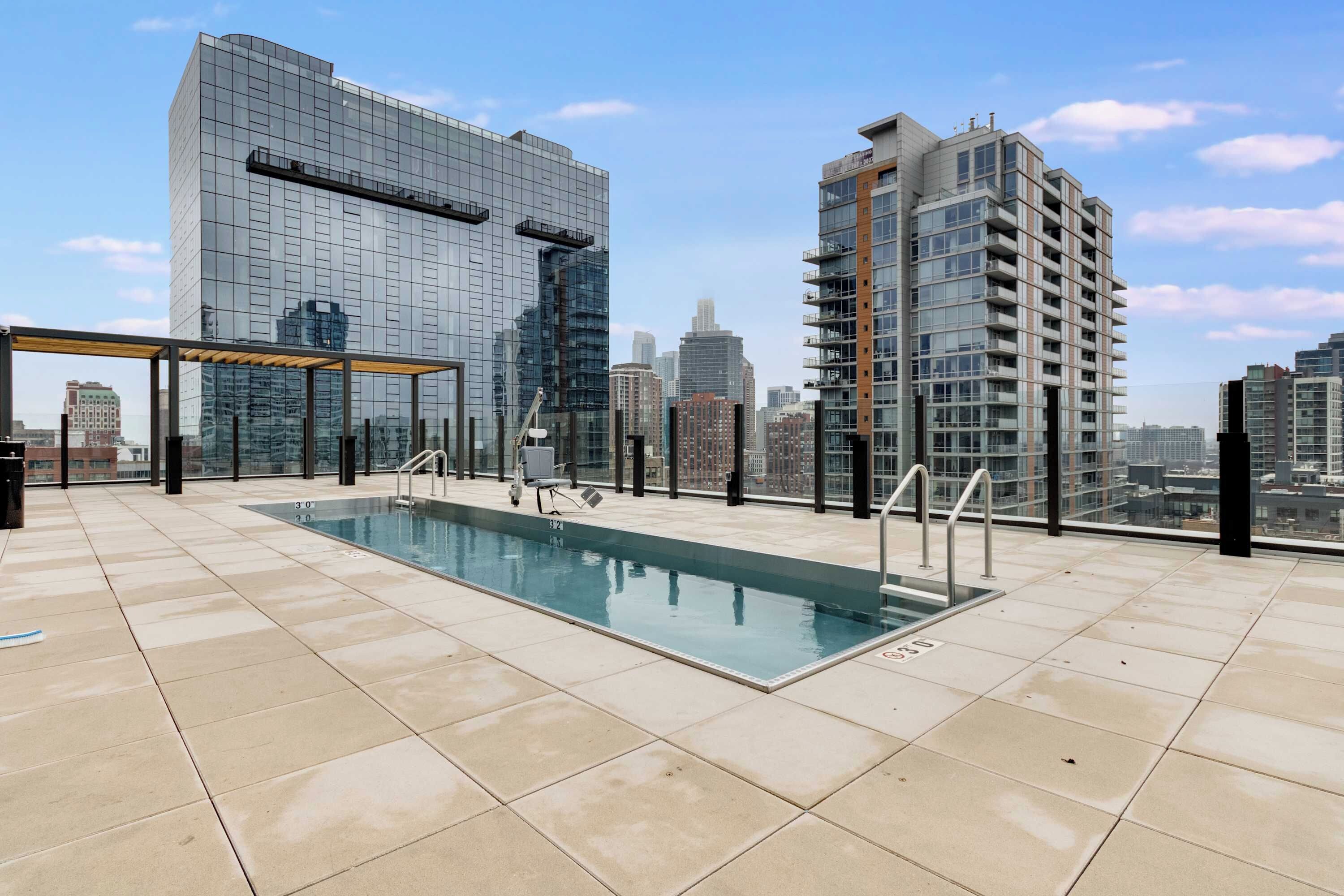 Una piscina en la azotea con cerramiento de vidrio, rodeada de edificios altos.