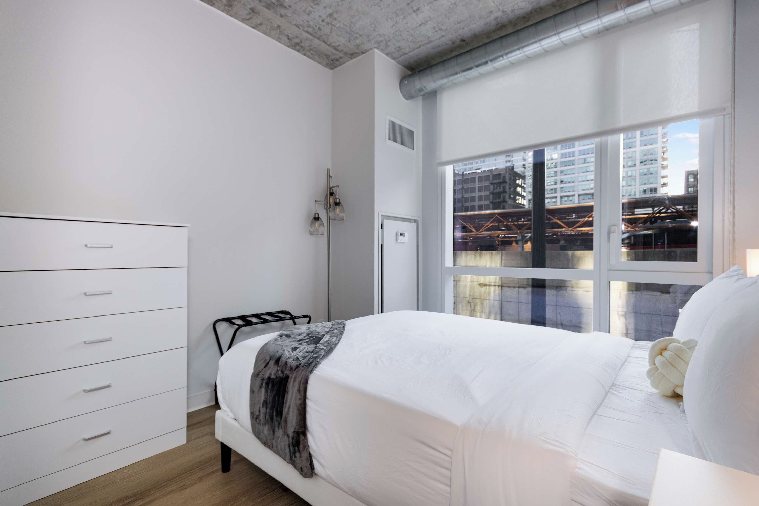 Quarto com cama, penteadeira, janela e vista para a cidade, além de radiador.