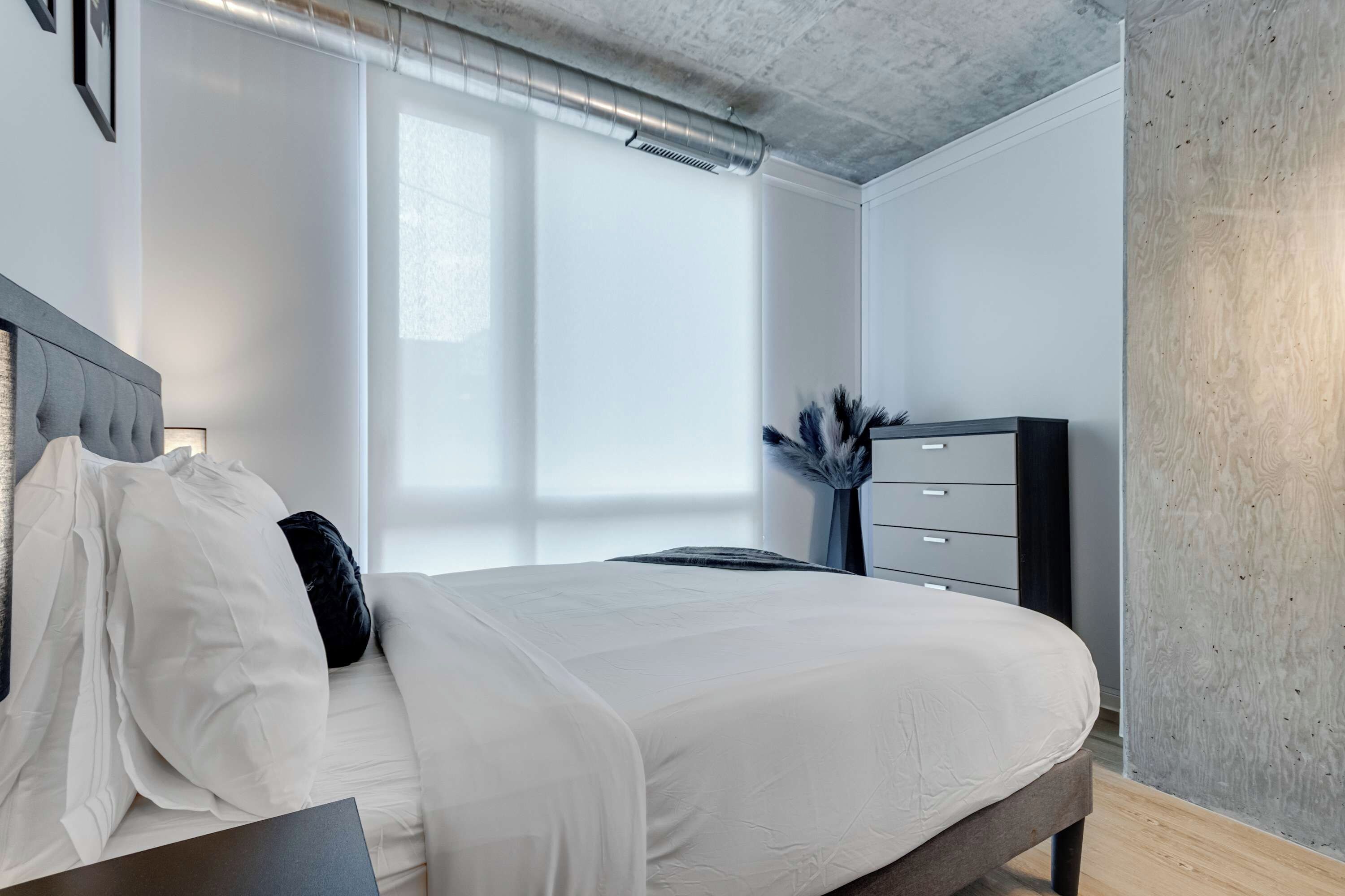Quarto moderno com cama, cômoda e uma janela grande.