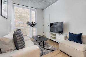 A modern living room with a sofa, a coffee table, a TV, and a large window. - South Loop Rooftop With In and Out Parking 6 (Chicago)