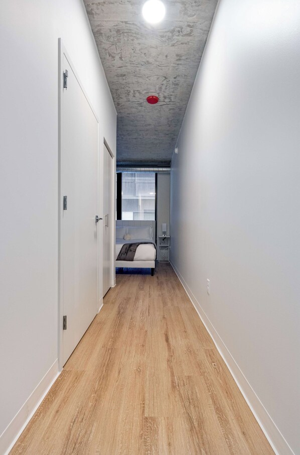 Een smalle gang met houten vloer, witte muren en een plafond met een ingebouwd verlichtingsarmatuur.