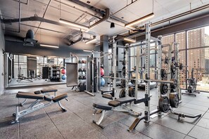 Uma academia com equipamentos de musculação, bancos e um espelho grande na parede.