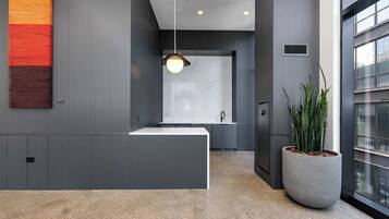 Uma área de recepção moderna, com um balcão branco, uma luminária pendente e uma grande planta em vaso.