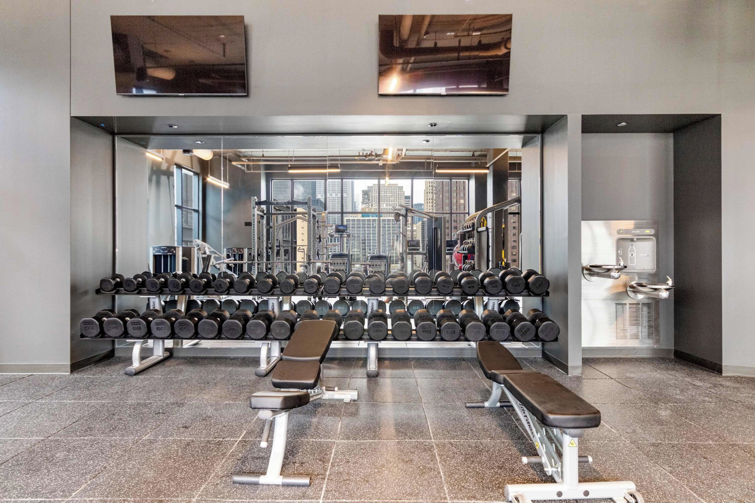 Uma academia com equipamentos de musculação, bancos e halteres.