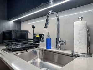 Cozinha moderna com pia de aço inoxidável, micro-ondas e dispensador de papel toalha.