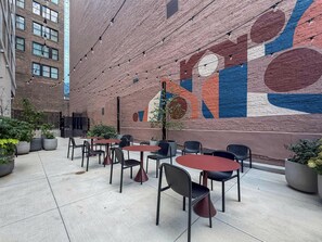 Een terras met tafels en stoelen, een bakstenen muur met een muurschildering en potplanten.