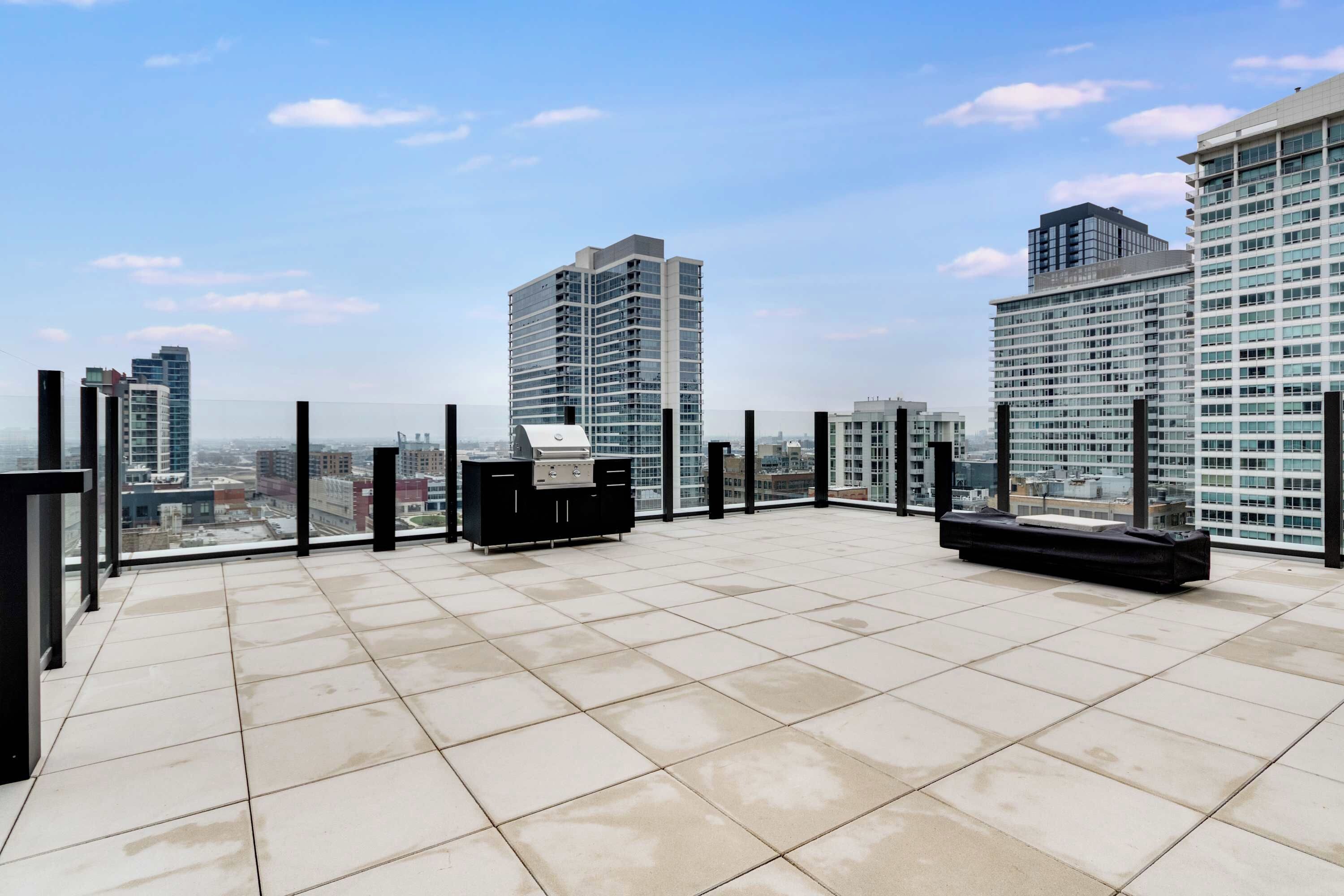 Terraço no telhado com churrasqueira, piso ladrilhado e vista dos edifícios altos ao redor.