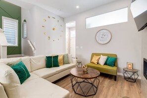 A modern living room with a sofa, a coffee table, and a green armchair. There is a wall clock and a framed quote on the wall. - 3FullBaths~PrivateYard~BBQ~5Beds (Calgary)