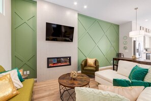 A modern living room with a flat-screen TV, a fireplace, a green accent wall, a leather armchair, and a dining area. - 3FullBaths~PrivateYard~BBQ~5Beds (Calgary)