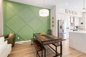 A modern kitchen with white cabinets, a stainless steel refrigerator, and a dining area with a wooden table and bench. - 3FullBaths~PrivateYard~BBQ~5Beds (Calgary)