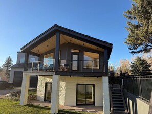 A modern two-story house with a balcony, large windows, and a stone facade. - Mountain Retreat w/ Pool & Mountain Views (Carbondale)