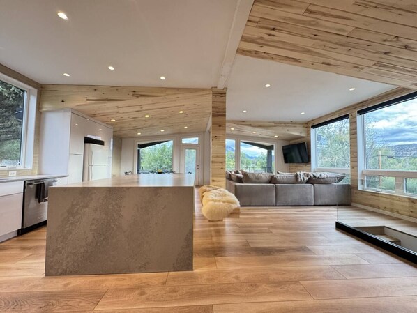 Un vaste espace de vie doté d’un grand plafond en bois, d’un îlot central et d’un coin salon offrant une vue sur l’extérieur.
