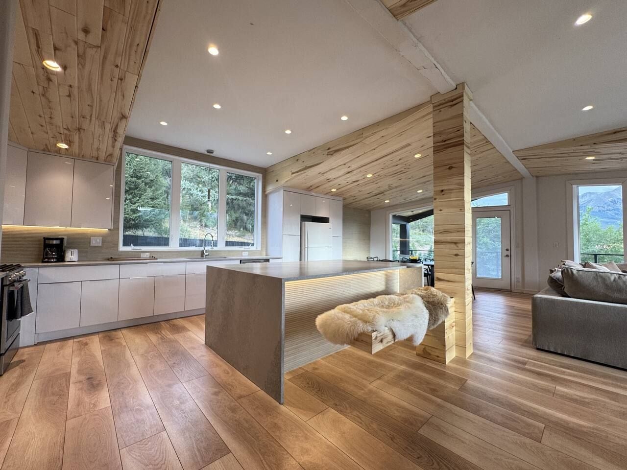 Una cocina moderna con una isla central, suelo de madera y ventanas amplias.