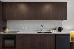 Une cuisine moderne avec des meubles de couleur bois foncé, un plan de travail blanc, un évier en acier inoxydable et un lave-vaisselle noir.