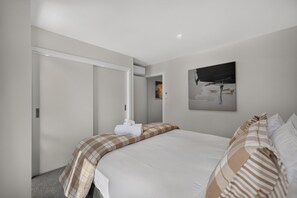 Une chambre d’hôtel avec un lit, une porte, un tableau et une serviette posée sur le lit.