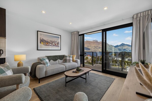 Un salon moderne avec un canapé, des fauteuils, une table basse et une grande fenêtre donnant sur les montagnes.