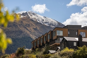 Un edificio moderno de varios pisos con grandes ventanales, con una montaña nevada y un cielo despejado de fondo.
