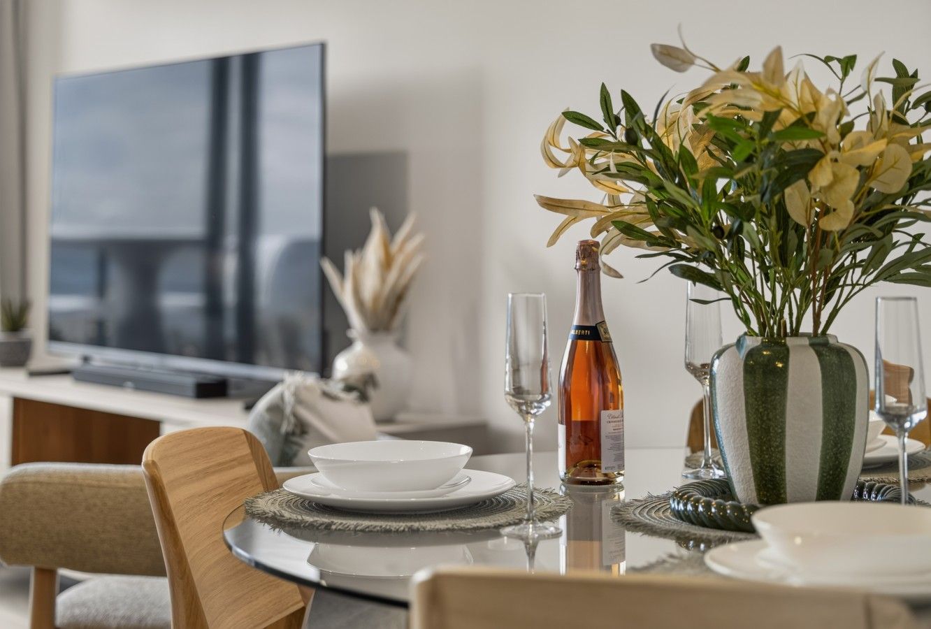 A dining table set with plates, a bottle, and glasses, with a television and decorative items in the background.