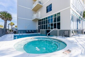 A swimming pool area with a hot tub, surrounded by a building with balconies and large windows. - Seawind 1808 | Gulf-front with Pools + Hot Tub (Gulf Shores)