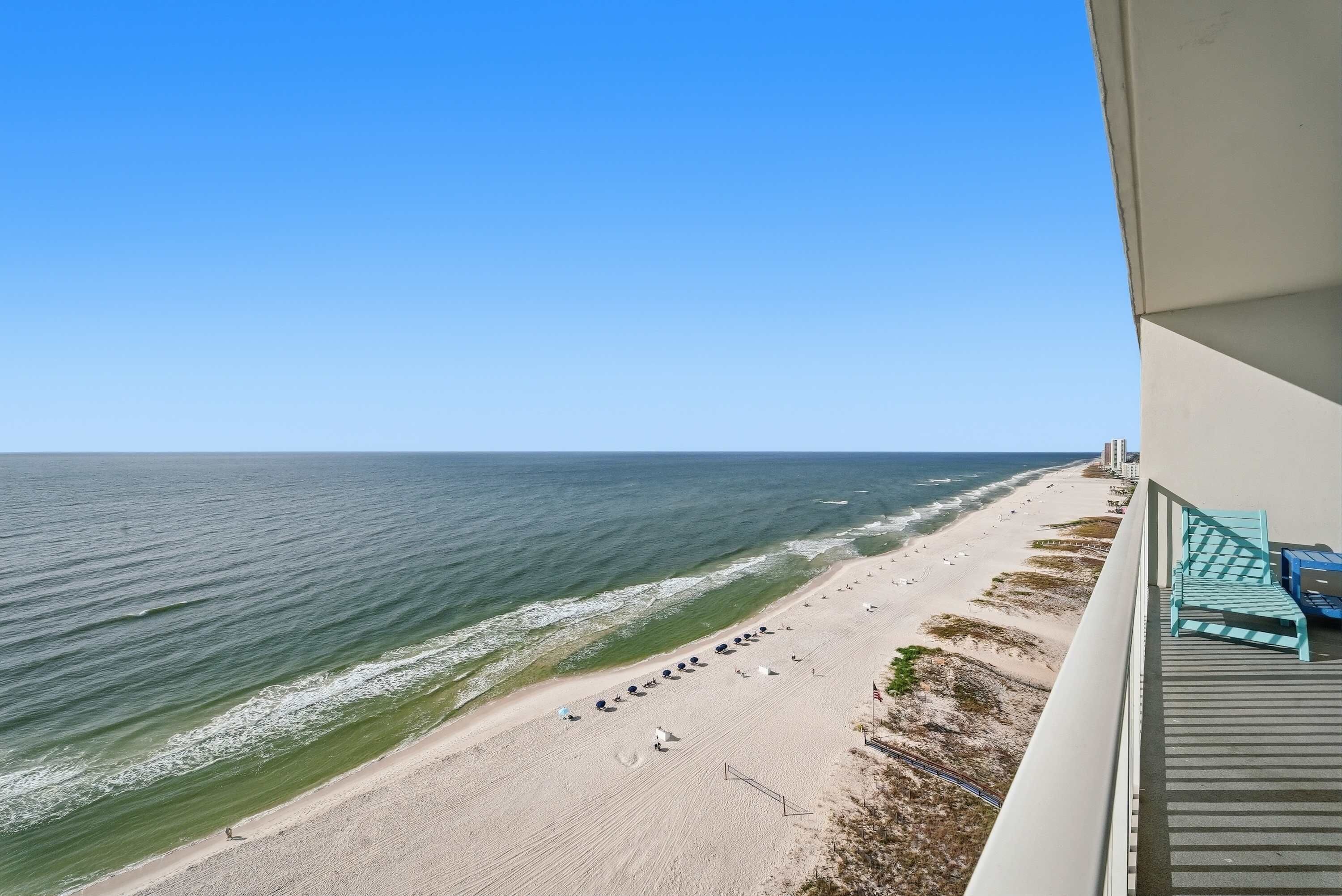 Strandudsigt fra en balkon med klar himmel, sandstrand og et par strandparasoller.
