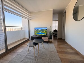 Ein modernes Wohnzimmer mit großem Fenster, einem Flachbildfernseher, einem kleinen schwarzen Tisch und einem Topf mit Pflanze.