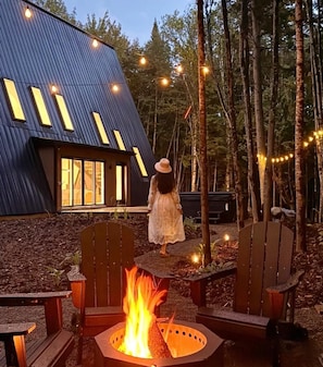 A modern building with a sloped roof and large windows, surrounded by a forest. - Cozy Peak | Luxury A-Frame | Hot Tub | Lake Access (Chertsey)
