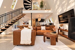 A modern living space with a staircase, a sofa set, a coffee table, and a television. - Cozy Peak | Luxury A-Frame | Hot Tub | Lake Access (Chertsey)