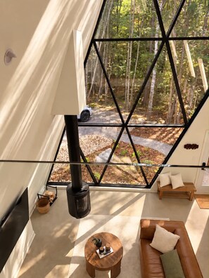 A modern interior with a large geometric window, a fireplace, a sofa, and a small round table. - Cozy Peak | Luxury A-Frame | Hot Tub | Lake Access (Chertsey)
