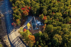 An aerial view of a secluded cabin surrounded by dense forest, with a clear road leading to it. - Cozy Peak | Luxury A-Frame | Hot Tub | Lake Access (Chertsey)