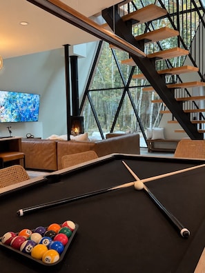 A modern living room with a pool table, a fireplace, and a staircase. - Cozy Peak | Luxury A-Frame | Hot Tub | Lake Access (Chertsey)