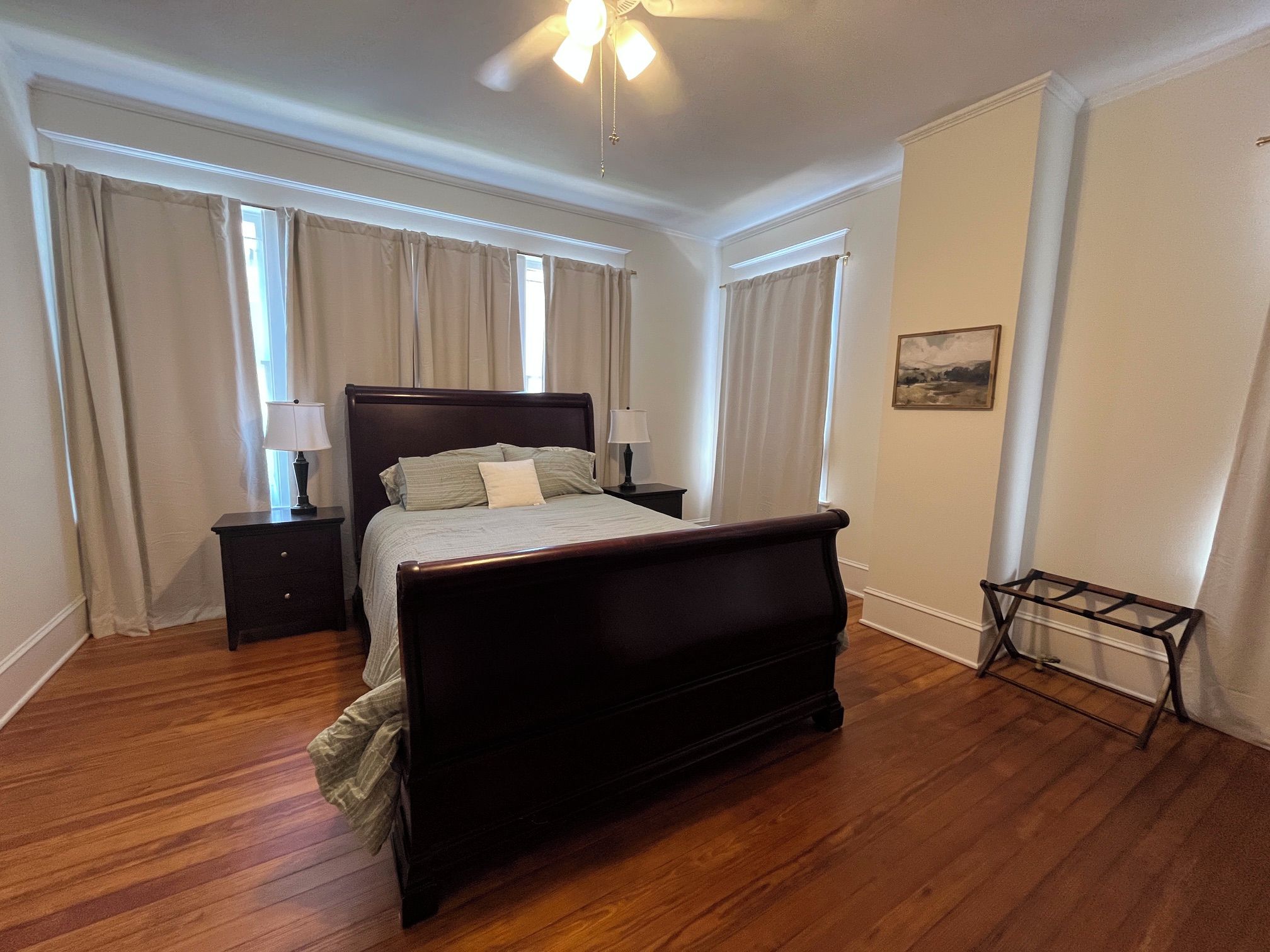 Een slaapkamer met een houten bed, twee nachtkastjes, een plafondventilator en een raam met gordijnen.