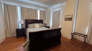 Een slaapkamer met een houten bed, twee nachtkastjes, een plafondventilator en een raam met gordijnen.