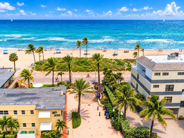 Un hotel frente al mar, con vista al océano, palmeras y una playa de arena.