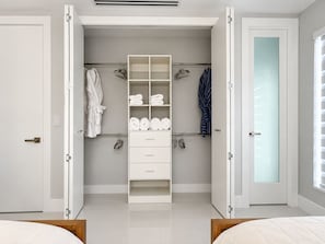 Quarto moderno com armário embutido, cama e banheiro com portas de vidro jateado.