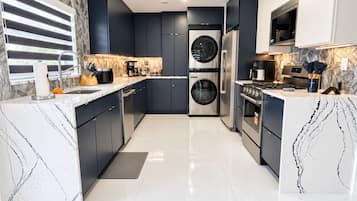 Una cocina moderna con armarios oscuros, un refrigerador de acero inoxidable, horno empotrado y una cafetera.