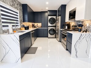 Una cocina moderna con armarios oscuros, un refrigerador de acero inoxidable, horno empotrado y una cafetera.