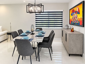 Uma área de refeições moderna com mesa retangular, cadeiras pretas e um lustre contemporâneo.