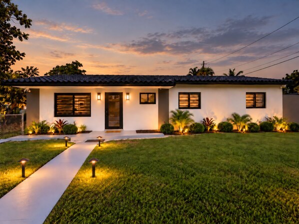 A modern two-story house with a flat roof, large windows, and a well-maintained lawn.