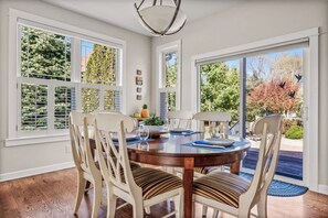 A dining area with a round table, chairs, and a view of trees through large windows. - Keppel Cove | Saugatuck • Hot Tub • Rec Room! (Saugatuck)