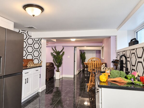 Una cocina moderna con una isla central, un comedor con una silla y una puerta visible que conduce a otra habitación.