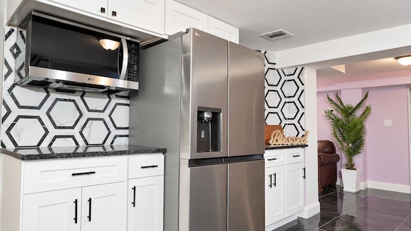 Une cuisine moderne dotée d’appareils électroménagers en acier inoxydable, de meubles blancs et d’un revêtement mural à motifs géométriques.