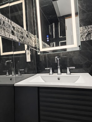 Une salle de bain moderne avec un grand miroir, deux vasques et un pare-baignoire en marbre.