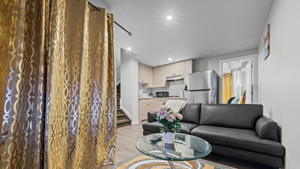 Ein modernes Wohnzimmer mit einem Glastisch, einer Couch und einer Küche im Hintergrund.
