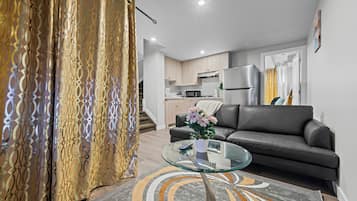 A modern living room with a glass coffee table, a sofa, and a kitchen in the background.