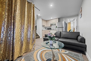A modern living room with a glass coffee table, a sofa, and a kitchen in the background.