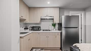 A compact kitchen with light wood cabinets, a stainless steel refrigerator, a microwave, and a gas stove.