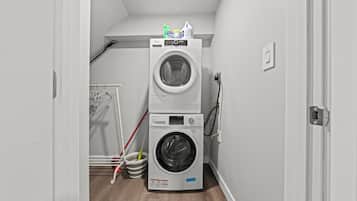 A laundry room with two stacked washing machines, a mop, and a broom.