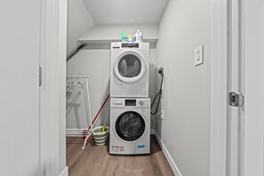A laundry room with two stacked washing machines, a mop, and a broom.