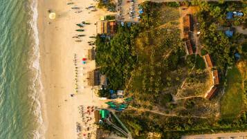 An aerial view of a beachside property with a parking area, beach umbrellas, and a road leading to the beach.