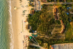 An aerial view of a beachside property with a parking area, beach umbrellas, and a road leading to the beach.